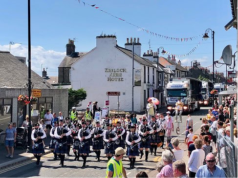 Local parade in Carnoustie with musicians and spectators on a sunny day.