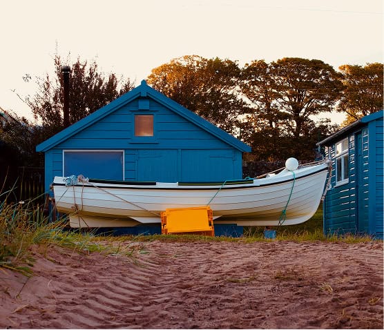 Colorful boat resting on sandy beach near blue wooden house.